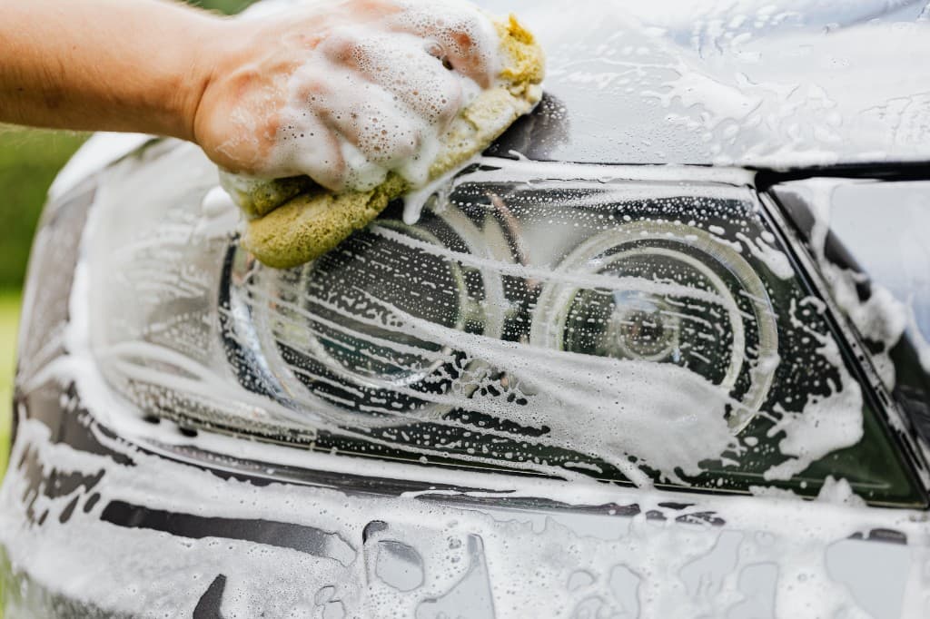 Professional hand-washing a car headlight with foam and sponge